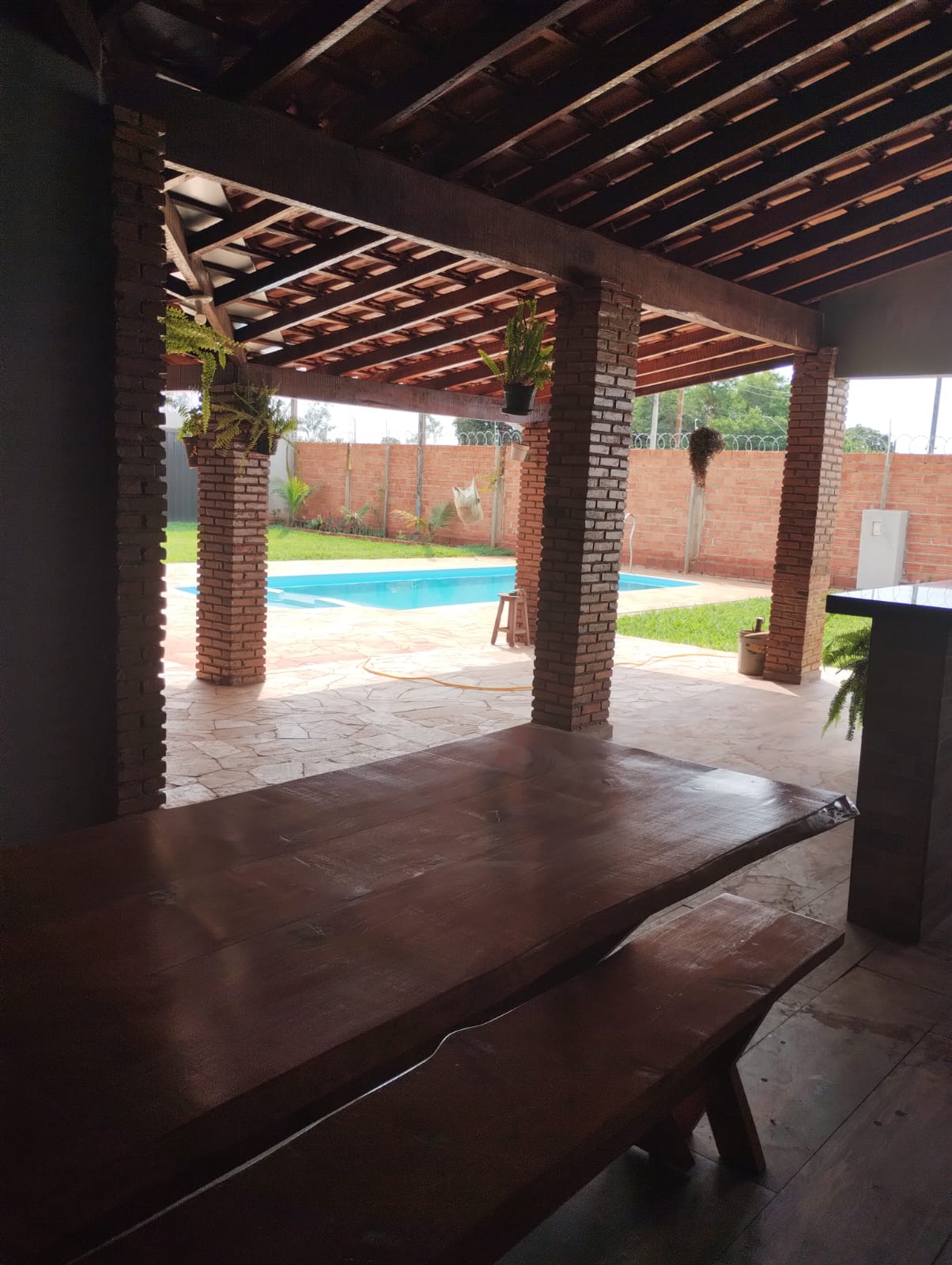 Área de estar coberta com mesa de madeira e vista pra piscina